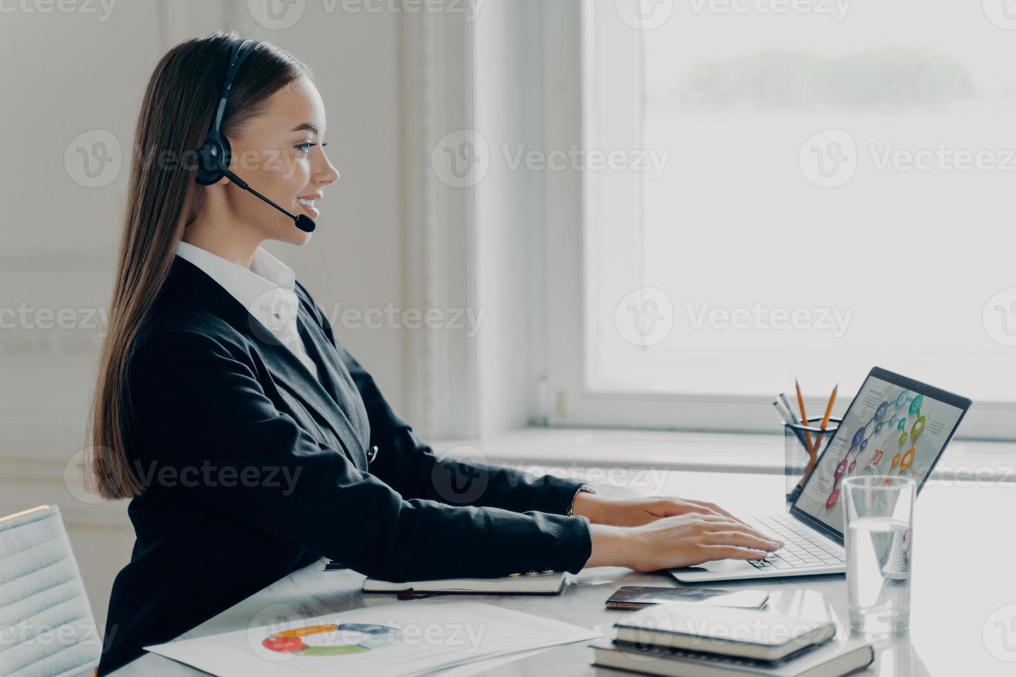 professionelle geschäftsfrau mit headset, die während des online-meetings mit finanzdaten arbeitet foto