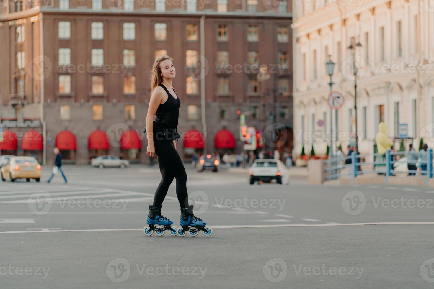 Ganzkörperaufnahme einer schlanken, dunkelhaarigen Frau, die auf einer asphaltierten Straße in schwarzer Sportkleidung rollt und Outdoor-Aktivitäten für einen gesunden und starken Körper genießt. sport- und hobbykonzept foto