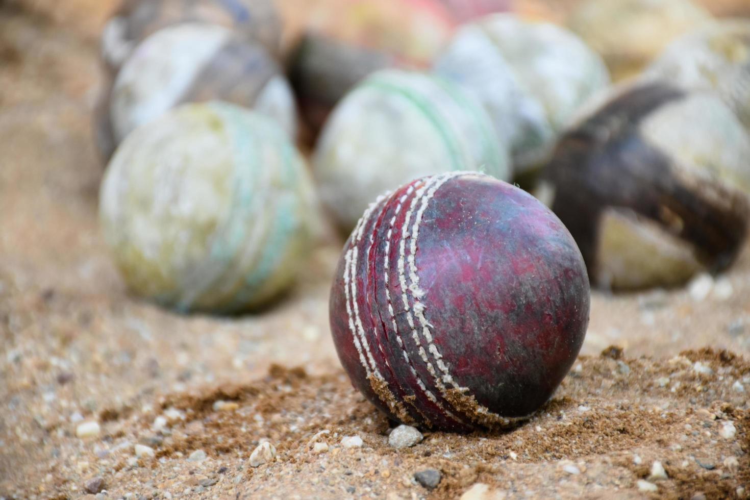 Alte lederne Cricketbälle zum Trainieren und Üben auf Sandboden neben dem Platz, weicher und selektiver Fokus auf rotem Cricketball. foto