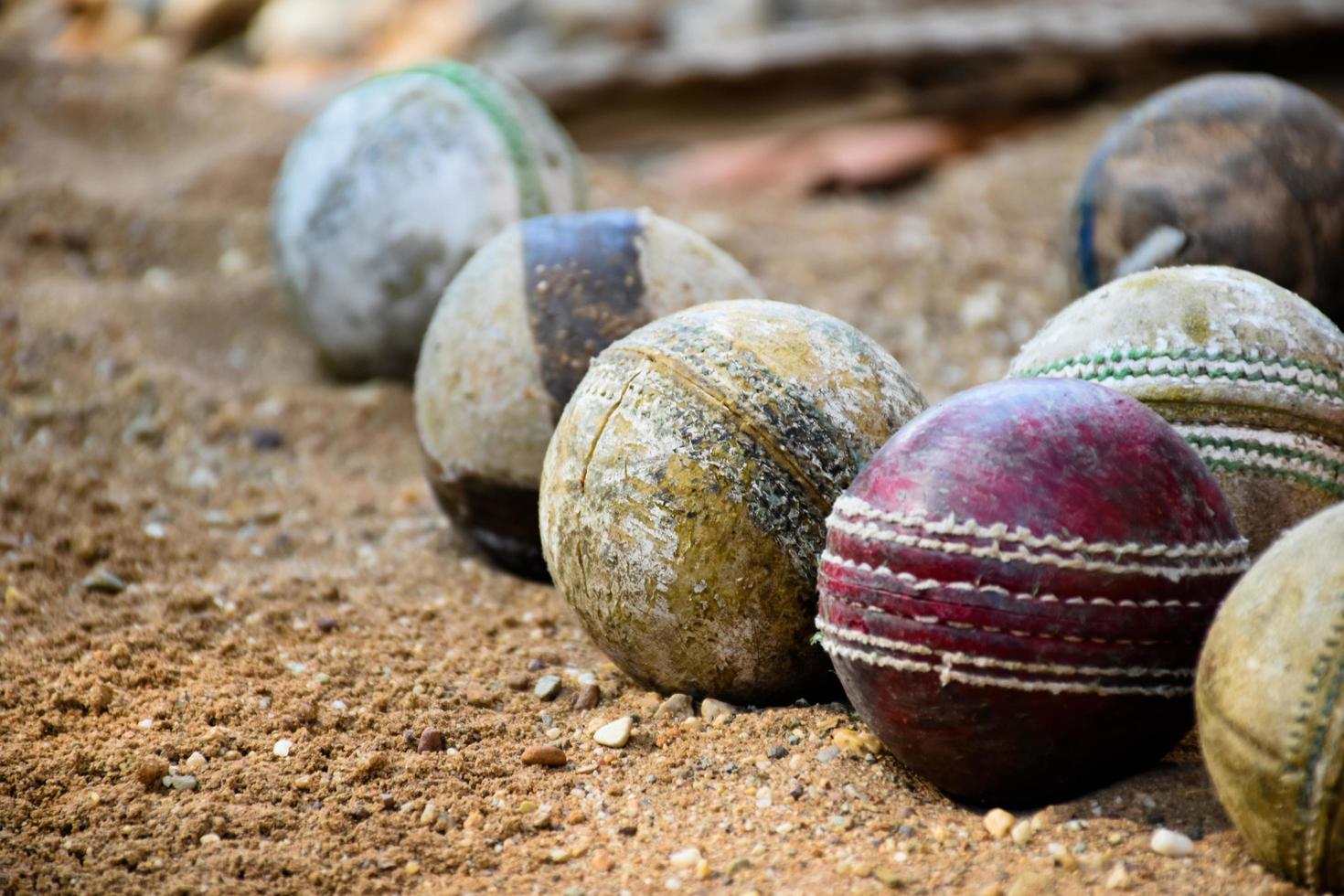 Alte lederne Cricketbälle zum Trainieren und Üben auf Sandboden neben dem Platz, weicher und selektiver Fokus auf rotem Cricketball. foto