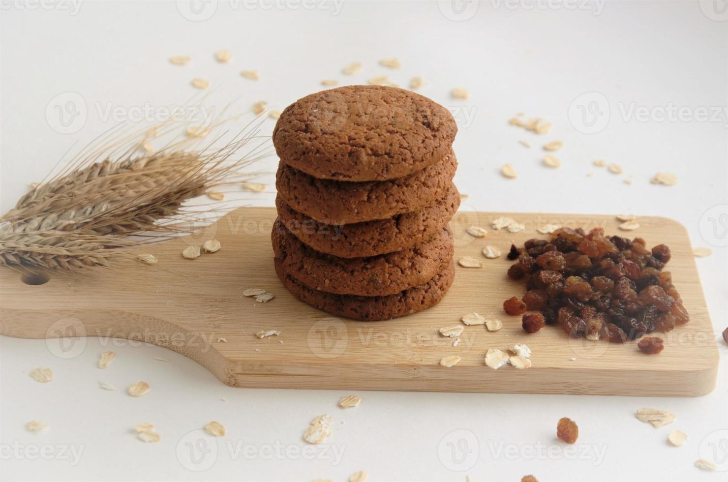 Kekse auf einem Holzbrett neben Rosinen und rohem Haferflocken, das Konzept von Haferkeksen mit Rosinen. hochwertiges Foto