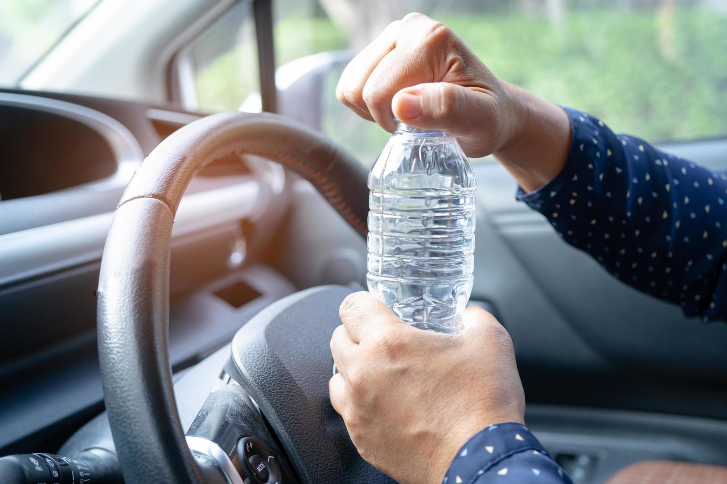 asiatische Fahrerin, die eine Flasche zum Trinken von Wasser hält, während sie ein Auto fährt. Wärmflasche aus Kunststoff verursacht Feuer. foto