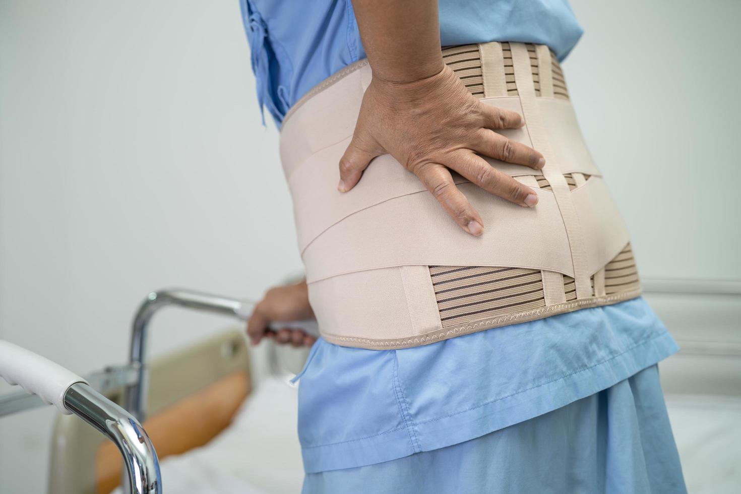 asiatische Patientin mit Rückenschmerzen-Unterstützungsgurt für orthopädische Lendenwirbelsäule mit Gehhilfe. foto