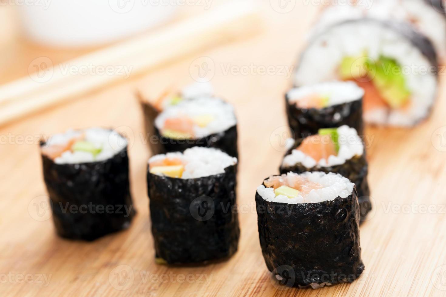 Sushi-Rollen mit Lachs, Avocado, Reis in Algen und Essstäbchen foto