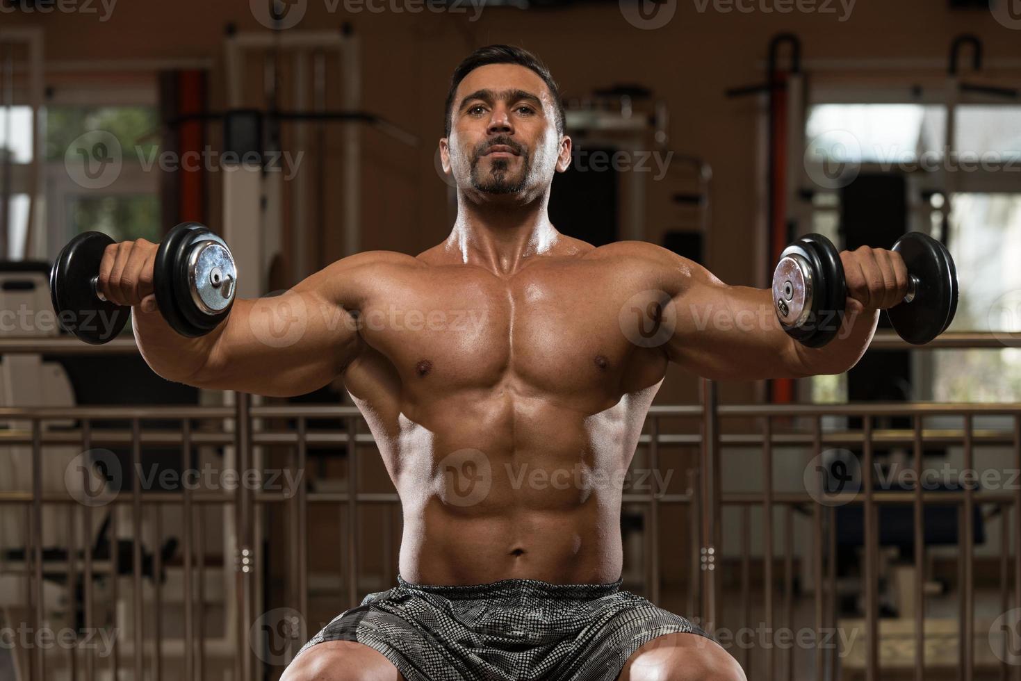 Bodybuilder, der schweres Gewicht für Schultern trainiert foto