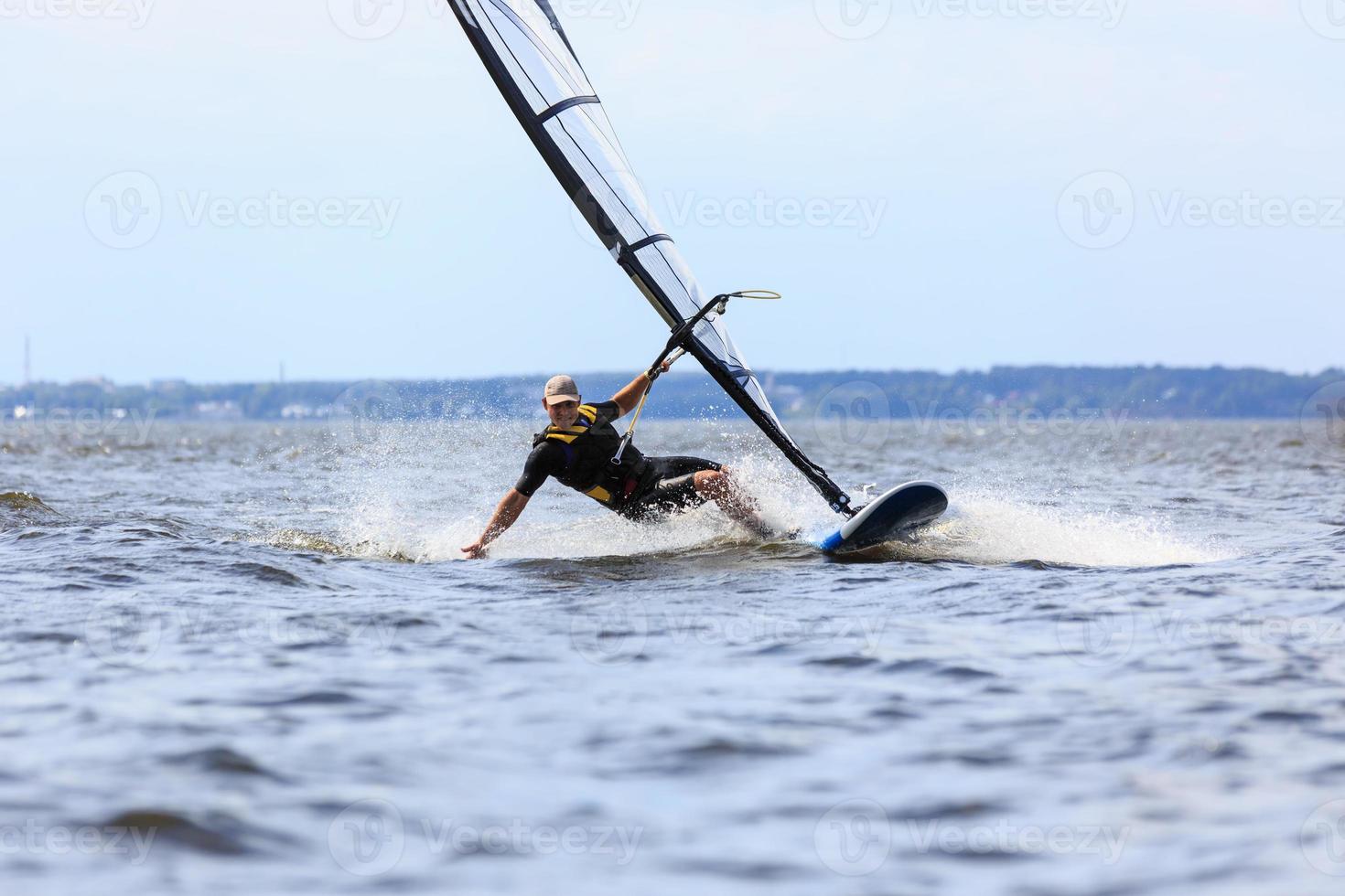 junger Mann, der den Wind in Wasserspritzern surft foto