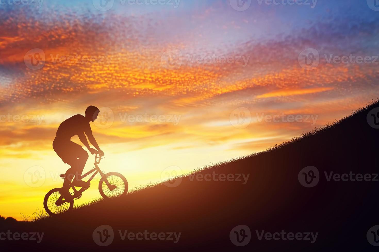 mann, der ein bmx-fahrrad bergauf gegen sonnenuntergangshimmel fährt. Kraft, Herausforderung. foto