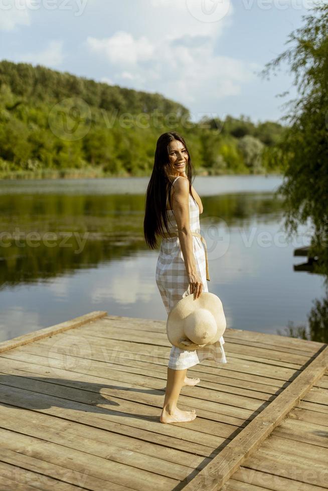 junge Frau, die auf dem Holzsteg am ruhigen See spazieren geht foto