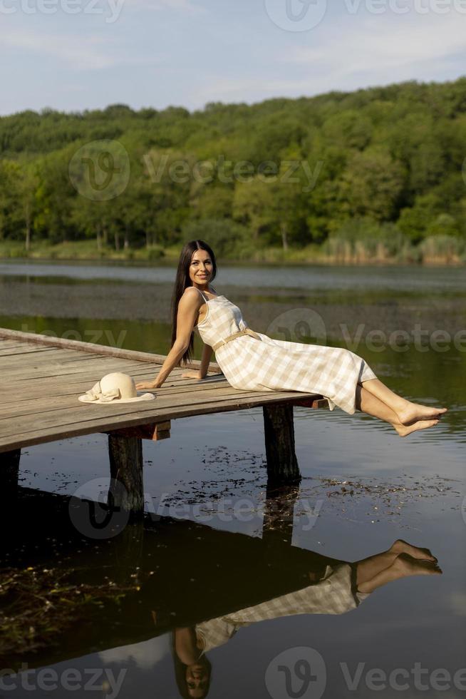 junge frau, die sich auf dem holzsteg am ruhigen see entspannt foto