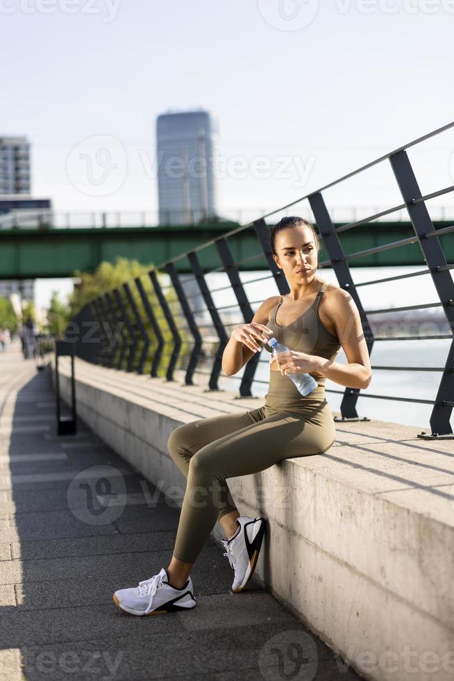 junge Frau macht eine Pause beim Sport auf der Flusspromenade foto