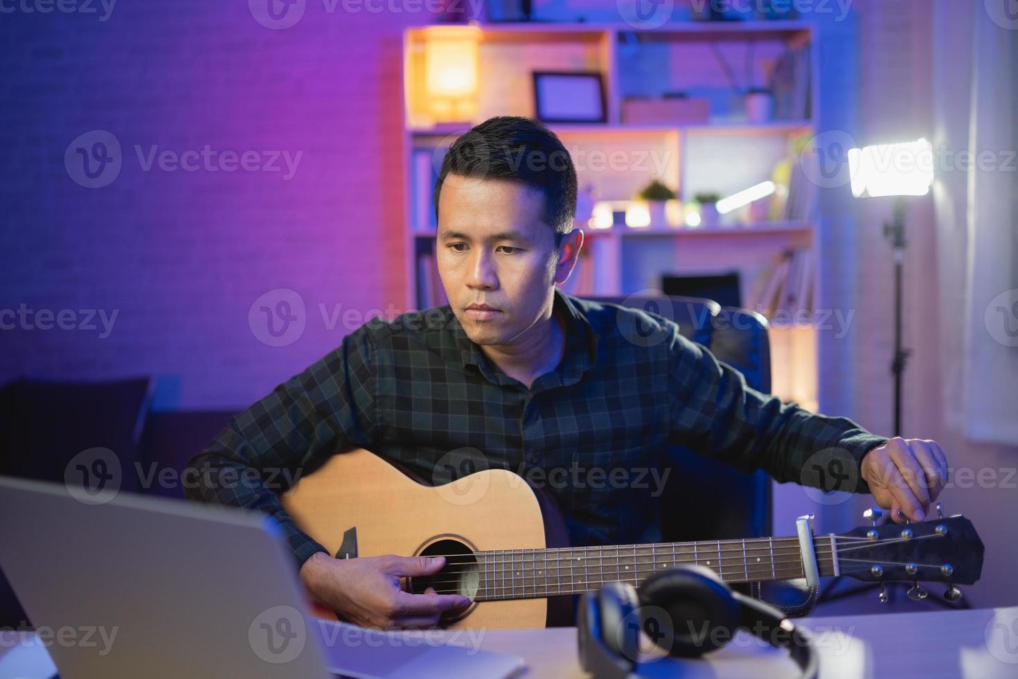 asiatischer mann youtuber live-streaming-performance gitarre spielen und ein lied singen. asiatischer mann unterrichtet gitarre und singt online. musiker, der musik mit laptop aufnimmt und akustikgitarre spielt. foto
