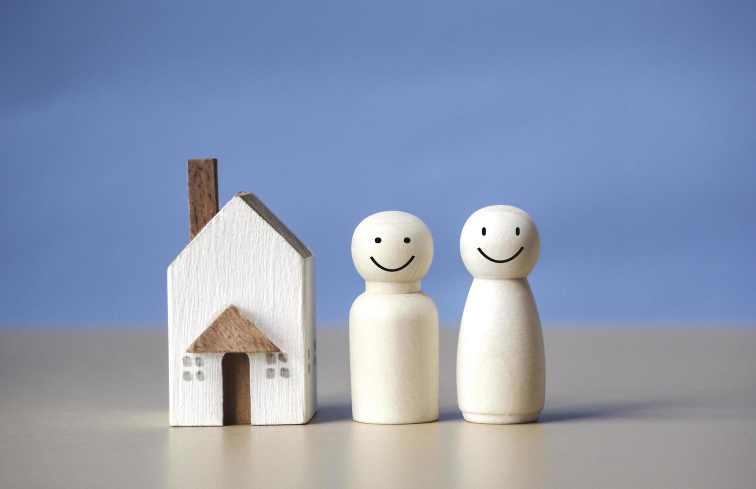 zwei Holzfiguren von Menschen mit Glück und ein Haus auf blauem Hintergrund. erschwinglicher wohnraum und hypotheken für den kauf von jungen familien und paaren. familiennest und kopierraum. foto