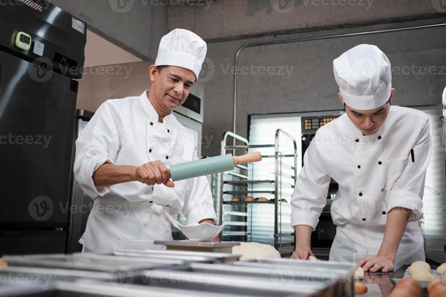 zwei professionelle asiatische männliche köche in weißen kochuniformen und schürzen kneten teig und eier, bereiten brot und frische backwaren zu und backen im ofen in der edelstahlküche des restaurants. foto