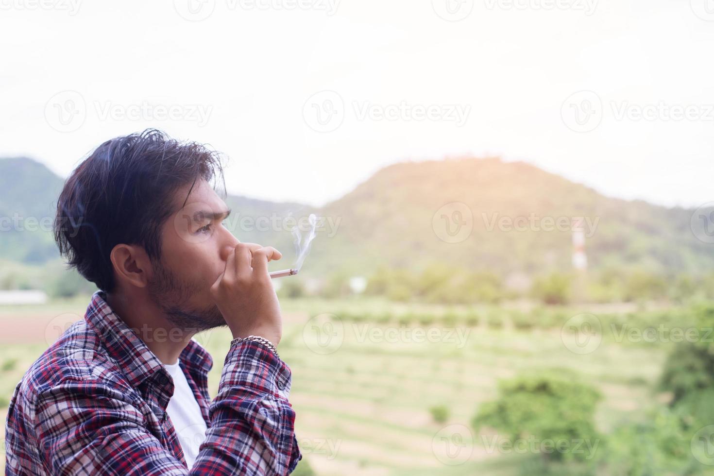 Hipster-Mann raucht Zigarette und steht hinter einem Berg. an der frischen Luft am Morgen. foto