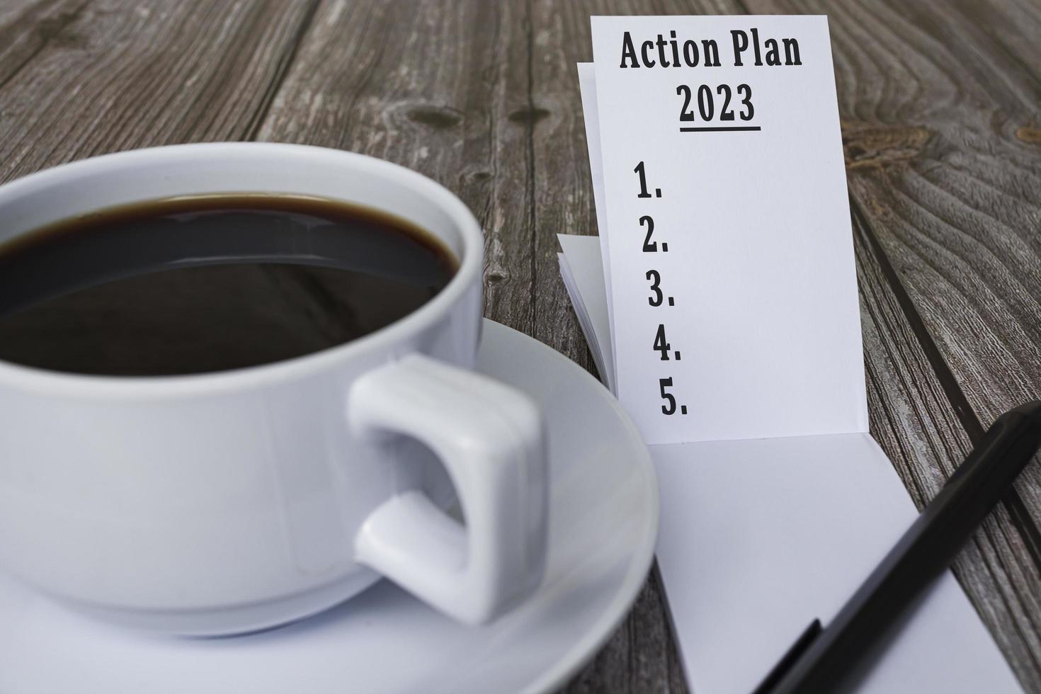 notizbuch mit aktionsplan 2023 text und kaffee auf holzschreibtisch. foto