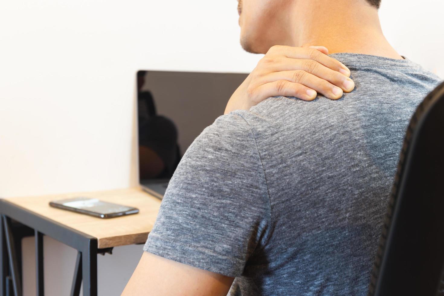 Mann mit Schulterschmerzen beim Arbeiten am Laptop. foto