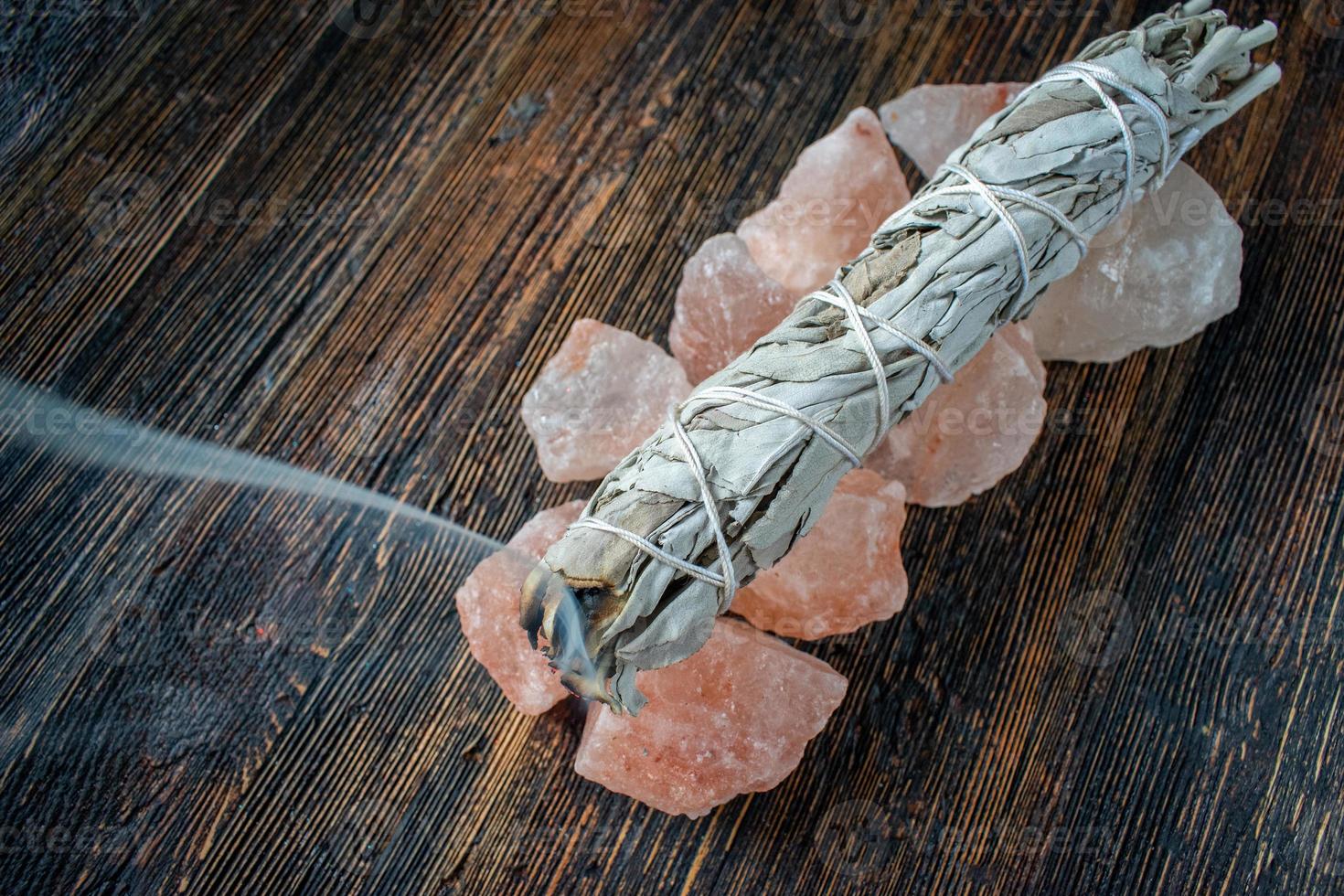 Brennen eines Salbei-Smudge-Sticks auf einer Basis aus rosa Salzkristallen mit Rauchspur foto