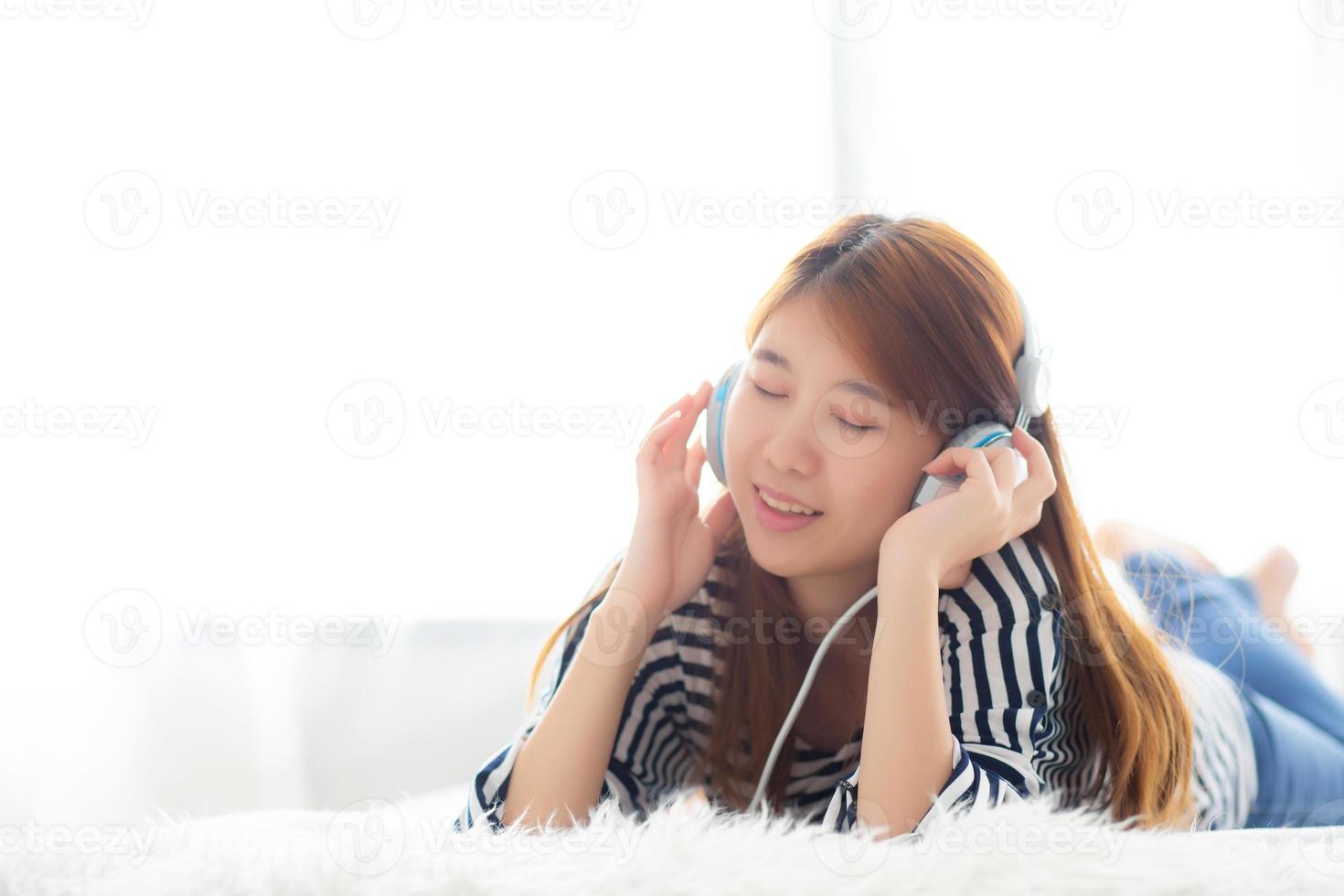 schöne asiatische junge frau genießen und spaß hören musik mit kopfhörer im schlafzimmer, mädchen entspannen mit kopfhörer, freizeit- und technologiekonzept. foto