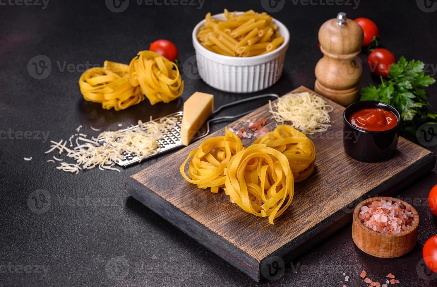 Rohe Tagliatelle-Paste mit geriebenem Käse, Kirschtomaten, Gewürzen und Kräutern auf einem Holzschneidebrett foto