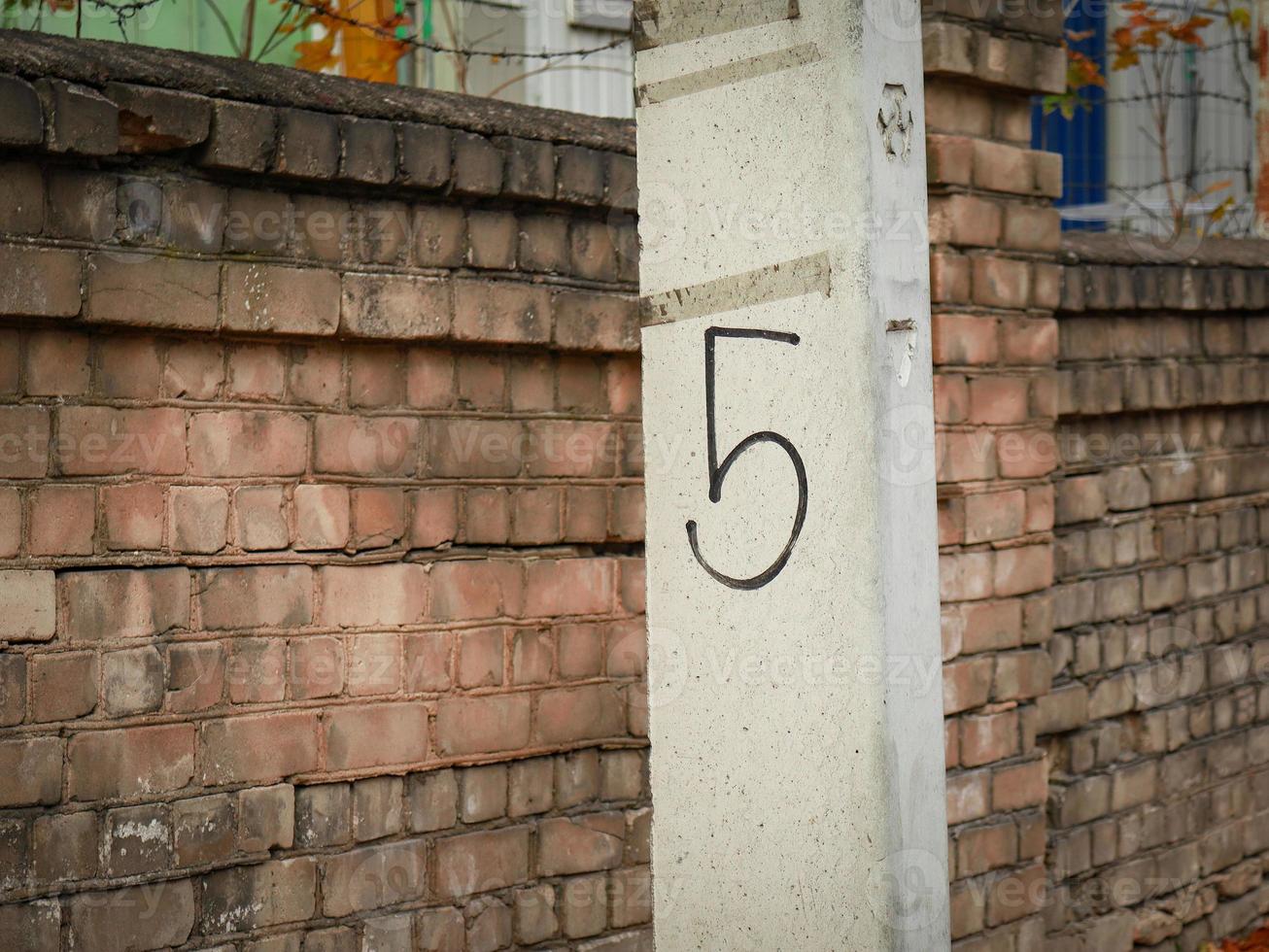 Nummer fünf handschriftlich in schwarzer Farbe auf Betonpfosten im Freien in der Nähe des braunen Ziegelmauerzauns foto