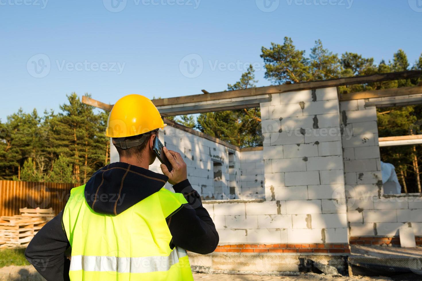 Bauarbeiter spricht auf einem Smartphone in einem gelben Hardhat