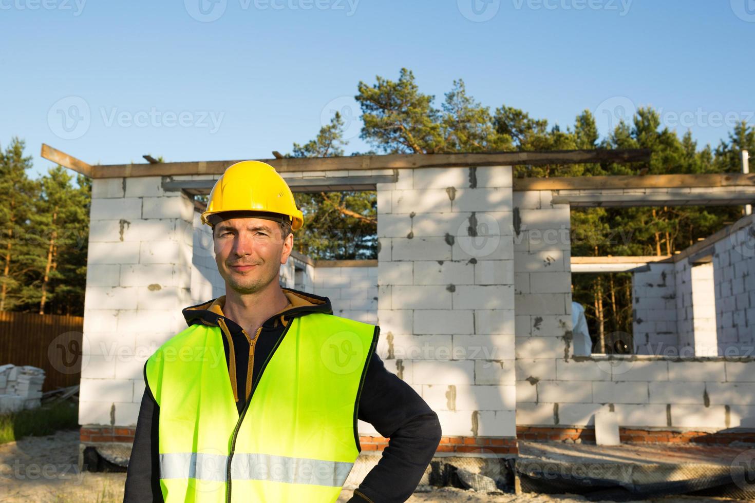 Bauarbeiter spricht auf einem Smartphone in einem gelben Hardhat und einer  reflektierenden Weste vor dem Hintergrund des Hausbaus - die Wände und  Fensteröffnungen bestehen aus porösen Betonblöcken. 8005302 Stock-Photo bei  Vecteezy