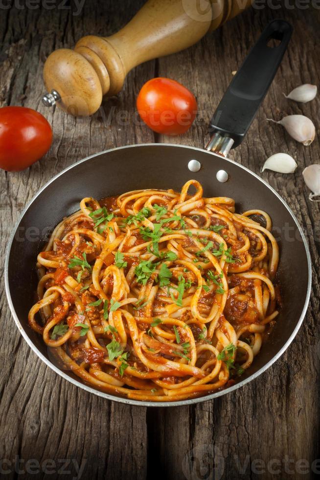 Spaghetti-Nudeln, Tomatensauce in einer schwarzen Pfanne sieht auf alten Holzbrettern köstlich aus, schwarzer Hintergrund. foto