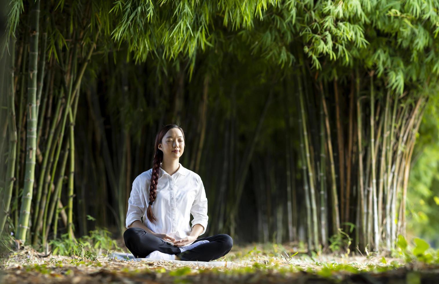Frau, die entspannend Meditation im Bambuswald praktiziert, um Glück aus innerer Friedensweisheit für ein gesundes Geist- und Seelenkonzept zu erlangen foto