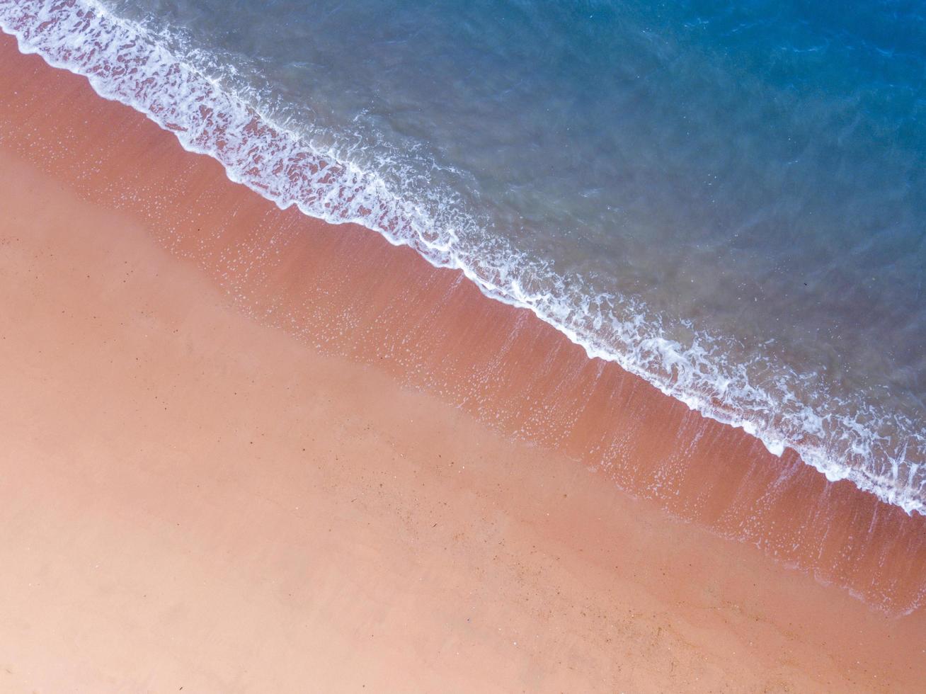 luftaufnahme des rosa sandstrandes mit tiefblauer meeresfarbe und weißer krachender welle im sommer mit kopierraum für reise- und urlaubskonzept foto