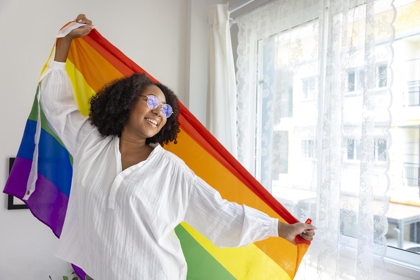 afroamerikanisches mädchen, das lgbtq-regenbogenfahne in ihrem schlafzimmer hält, um aus dem schrank zu kommen, und stolzmonatsfeier, um sexuelle vielfalt und gleichberechtigung in der homosexuellen orientierung zu fördern foto