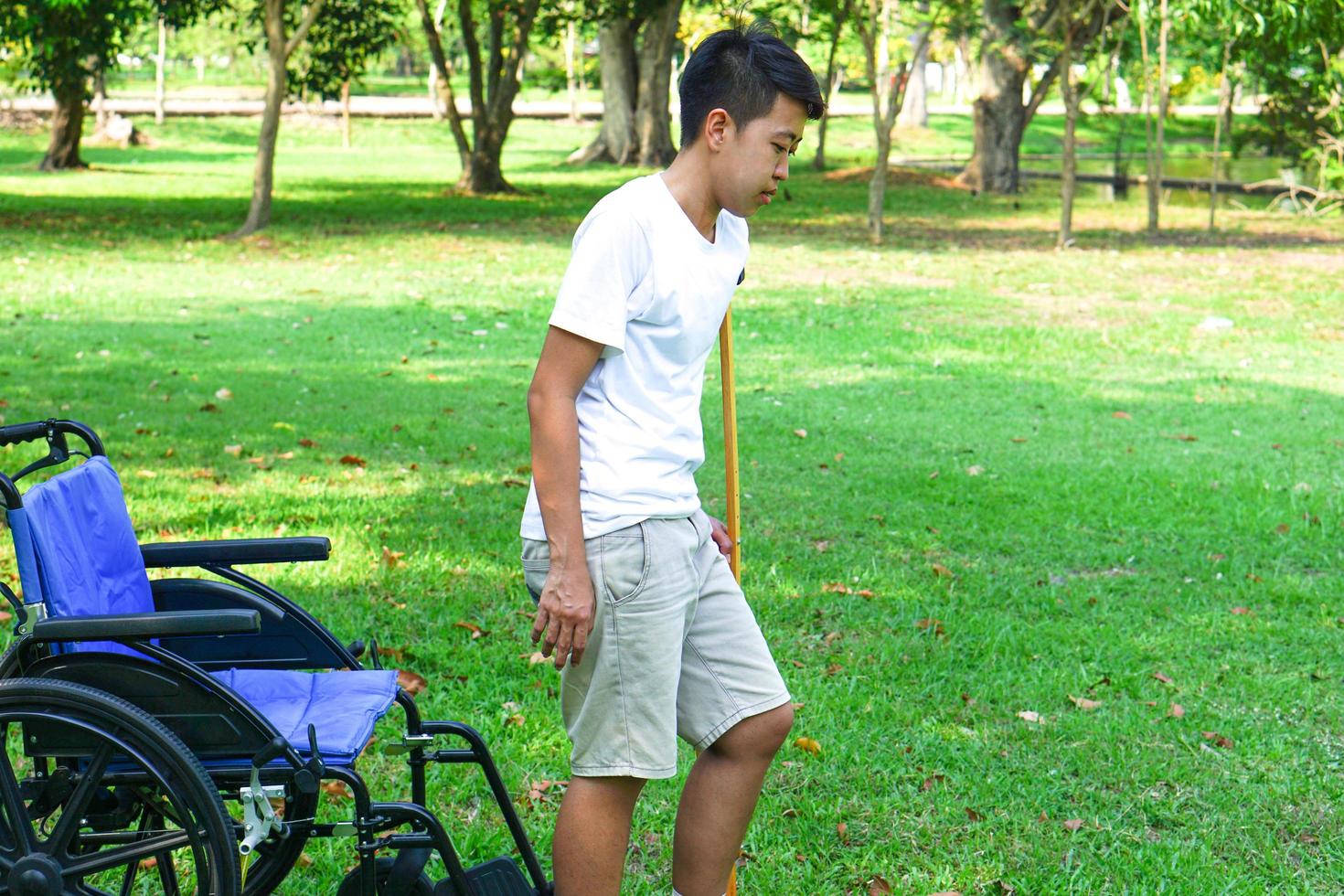 Der Patient stieg aus dem Rollstuhl und benutzte eine Krücke, um ihn beim Gehen auf dem Rasen zu unterstützen. gesundheitswesen und medizinisches konzept. foto