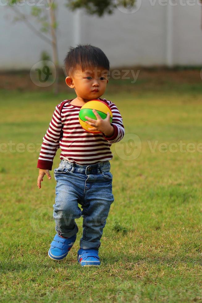 asiatischer Junge, der im Park Fußball spielt. Kind mit Ballspielzeug auf der Wiese. foto