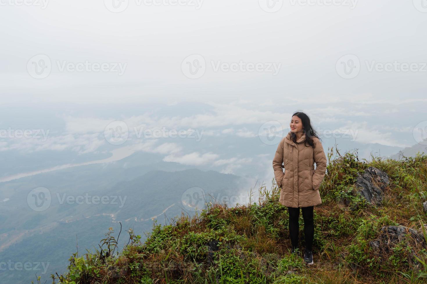 asiatische frau im wintermantel, die auf berggipfel am pha tang aussichtspunkt 103 mit flussblick und meeresnebel und dichtem nebelhimmel steht. reiseort in chaing rai, thailand foto