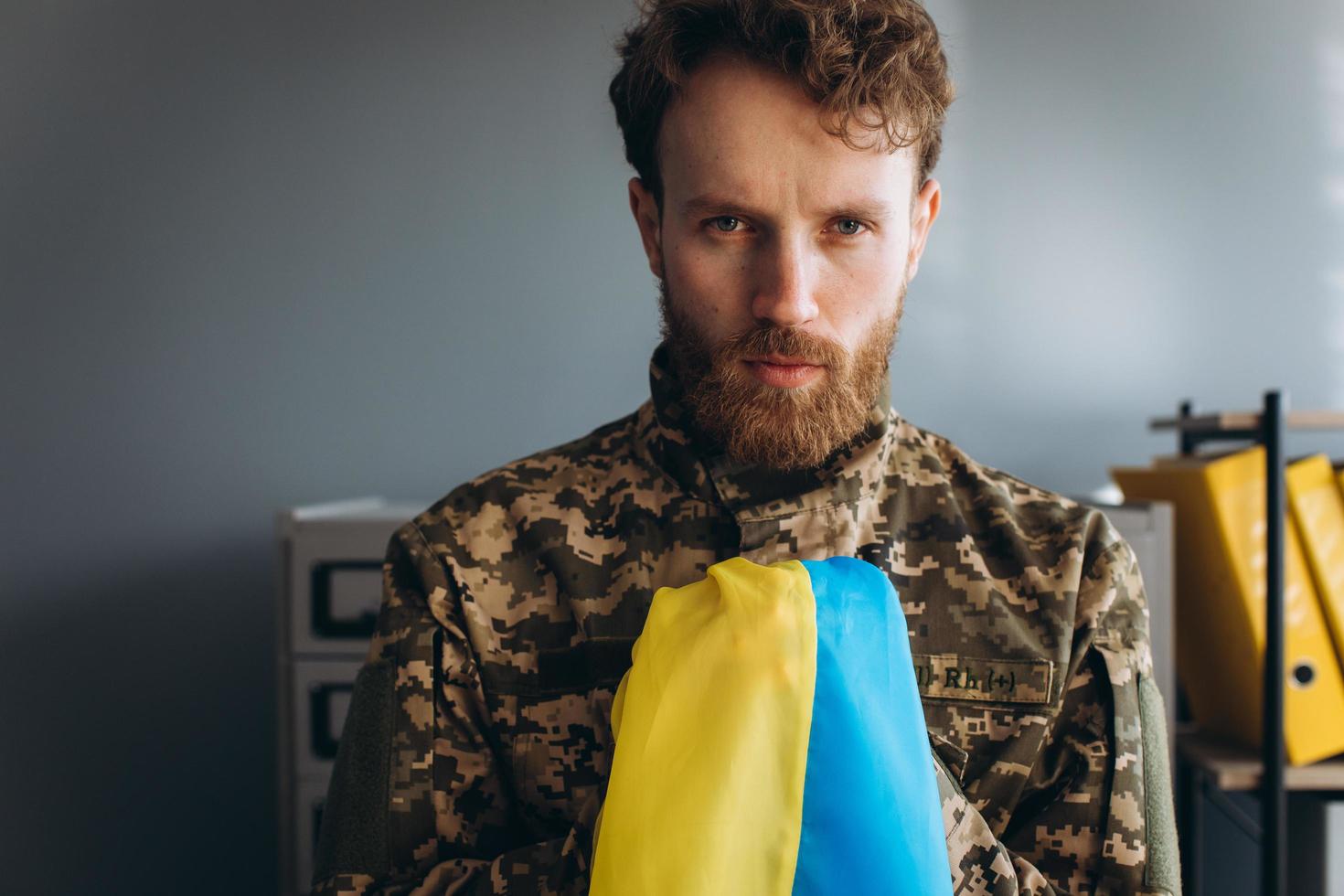 ukrainischer patriot soldat in militäruniform, der eine gelbe und blaue flagge im büro hält foto