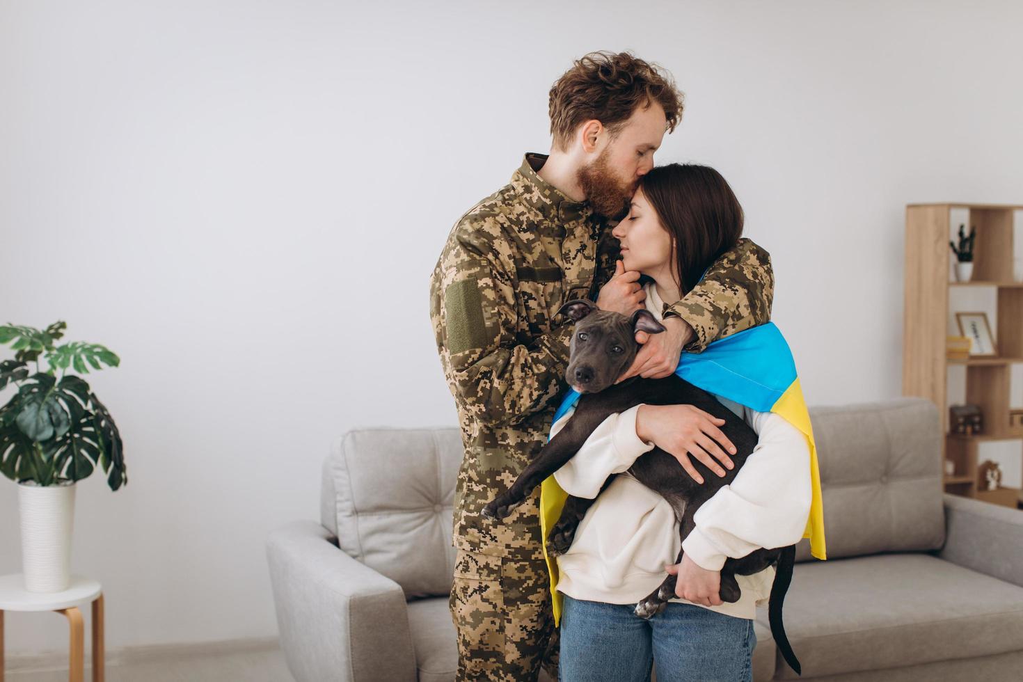 ein ukrainisches paar, ein soldat in militäruniform und ein mädchen, das in eine ukrainische flagge gehüllt ist, halten einen hund in ihren armen, glücklich zusammen. foto