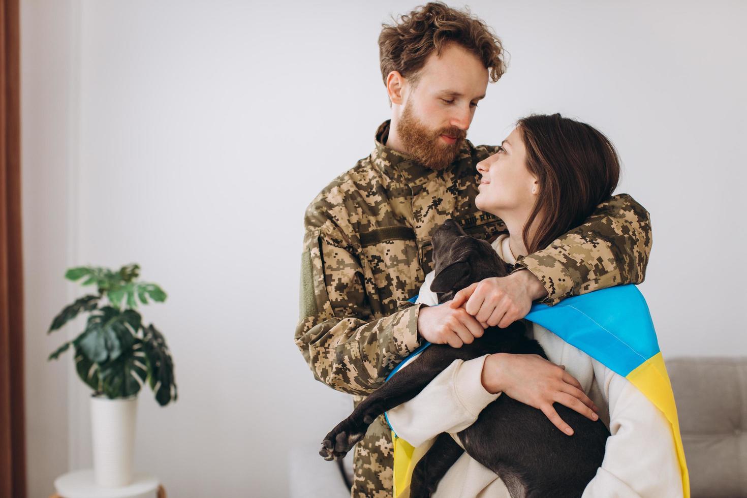 ein ukrainisches paar, ein soldat in militäruniform und ein mädchen, das in eine ukrainische flagge gehüllt ist, halten einen hund in ihren armen, glücklich zusammen. foto