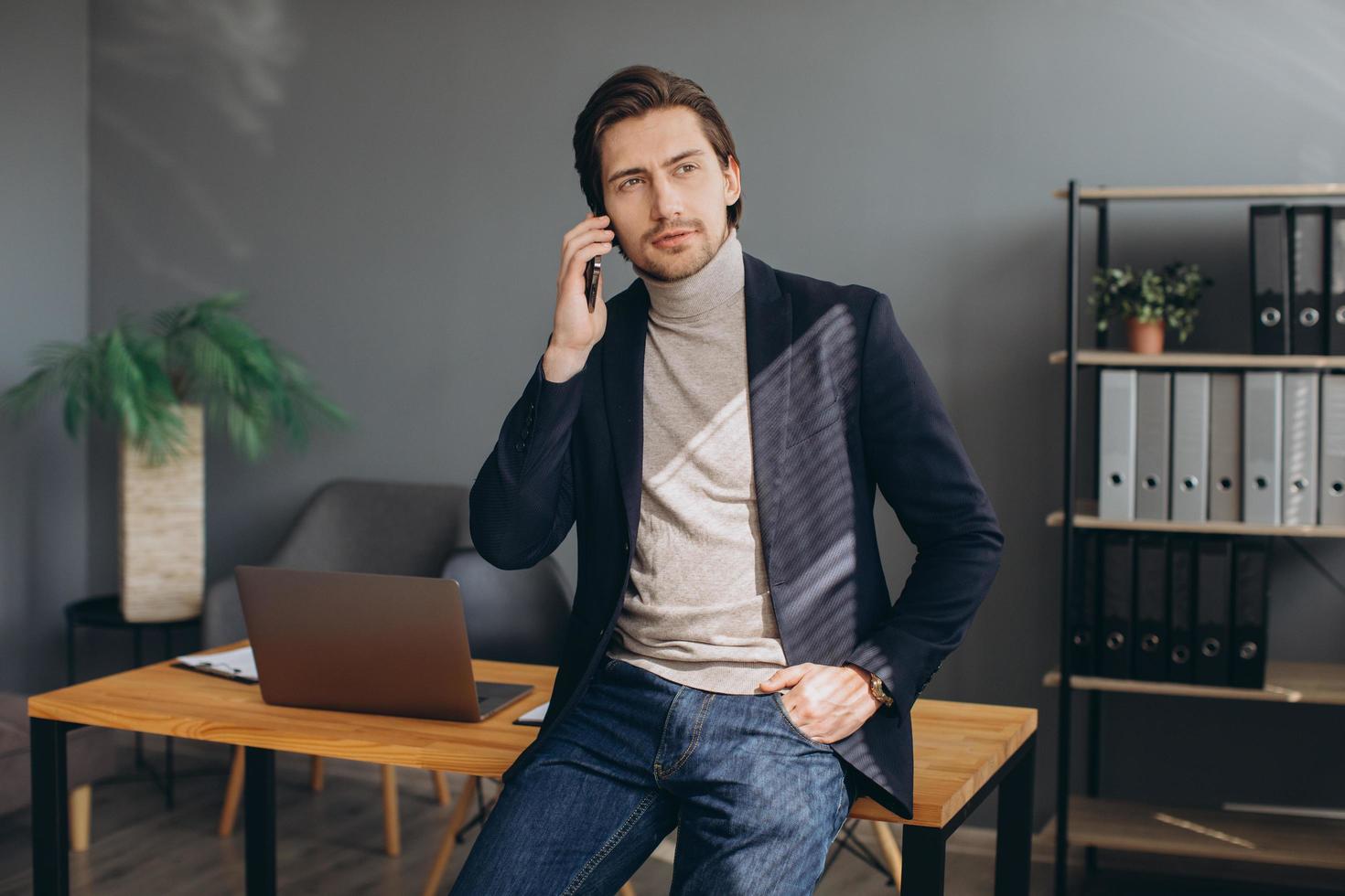 Schöner Geschäftsmann im Anzug, der im modernen Büro telefoniert foto