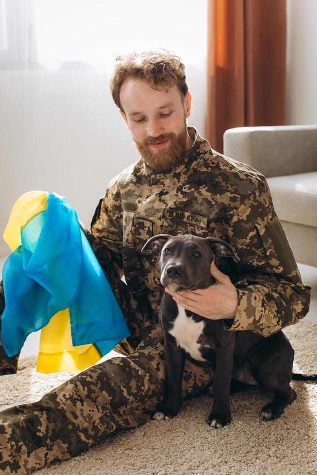 ukrainischer soldat umarmt und wickelt die ukrainische flagge seines treuen freundes um einen amstaff-hund im büro foto