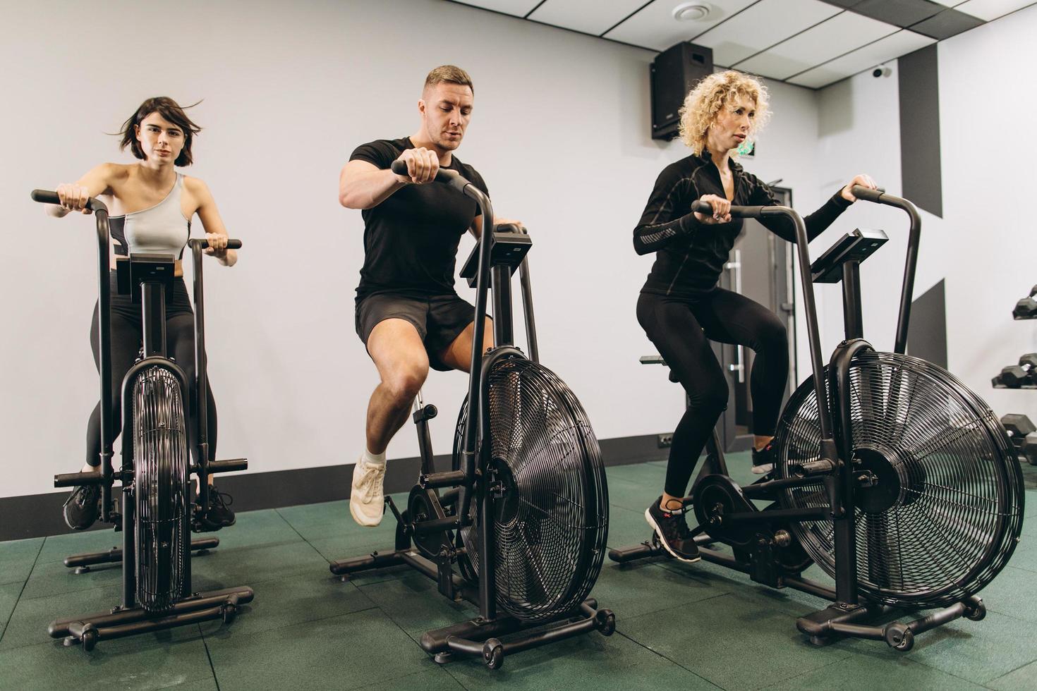 junger mann und frauen, die air bike für cardio-training im cross-trainingsstudio verwenden foto