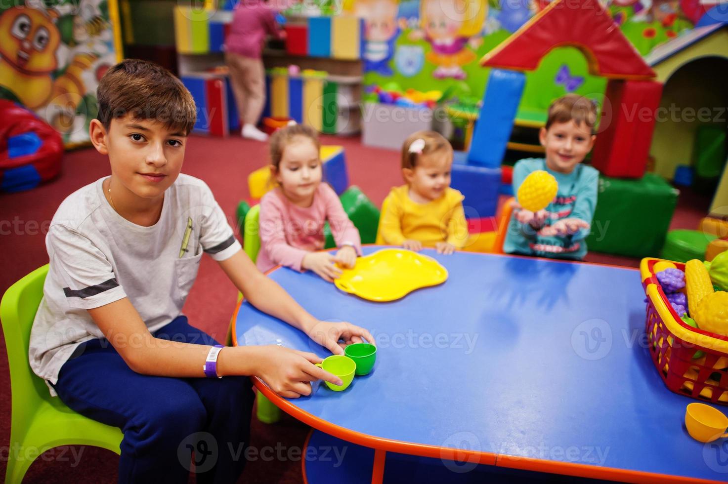 Vier Kinder spielen im Indoor-Spielzentrum. Kindergarten oder Vorschulspielzimmer. mit Plastikfrüchten am Tisch sitzen. foto