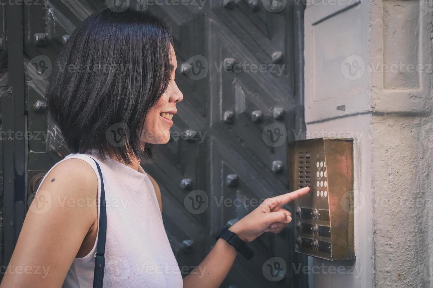 Mädchen, das im Freien vor einer riesigen antiken Tür einen Knopf der Haussprechanlage drückt. foto