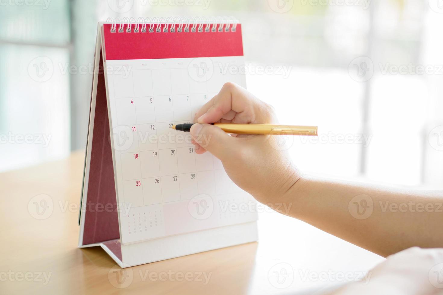 Frauenhand, die Kalender trägt und mit dem Stift darauf zeigt foto