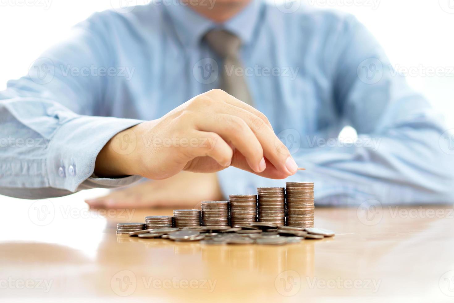 Geschäftsmann sitzt am Schreibtisch und stapelt Münzen foto