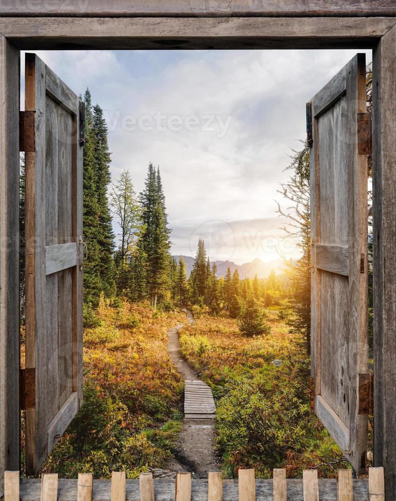 antike Holzfenster öffnen sich bei Sonnenaufgang zur herbstlichen Wildnis foto