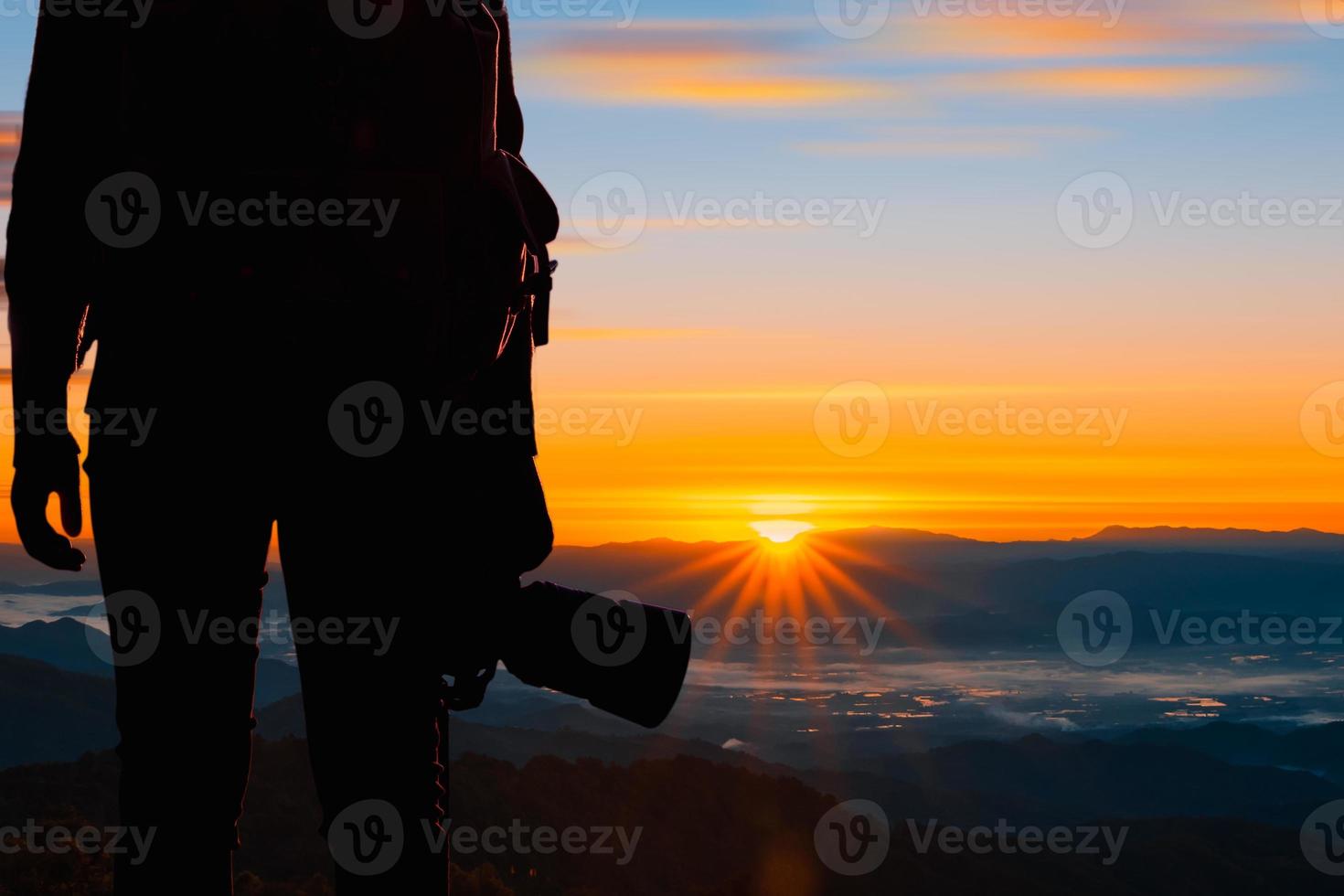 junger hipster-fotograf, der die kamera mit sonnenuntergang auf natürlichem berghintergrund hält. foto