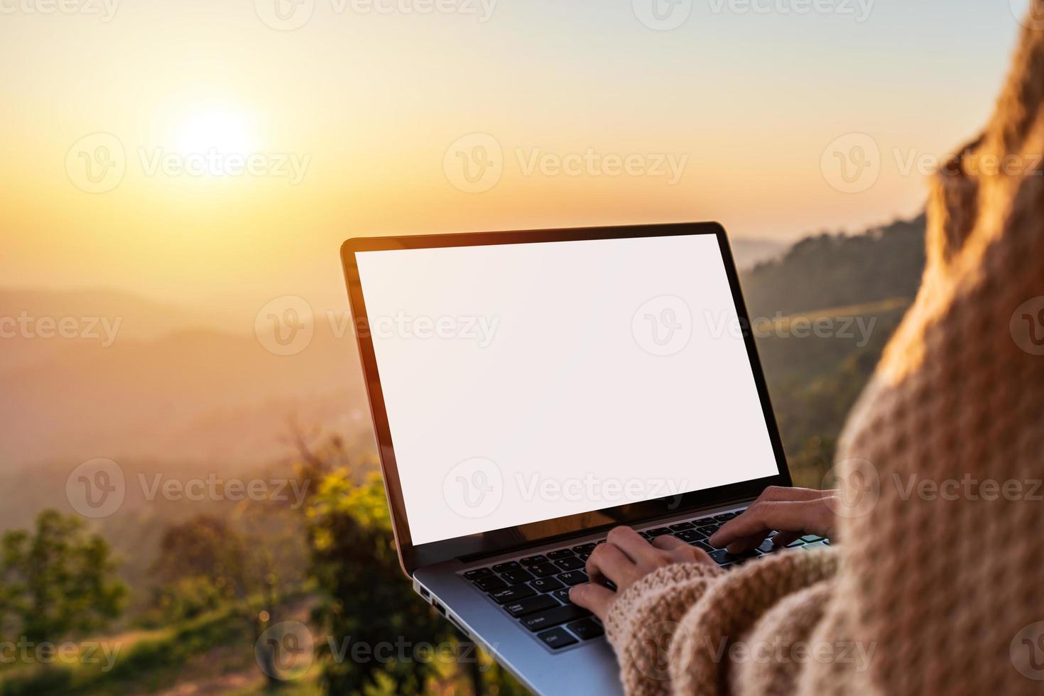 junge freiberufliche reisende, die online mit laptop arbeitet und die wunderschöne naturlandschaft mit bergblick bei sonnenaufgang genießt foto