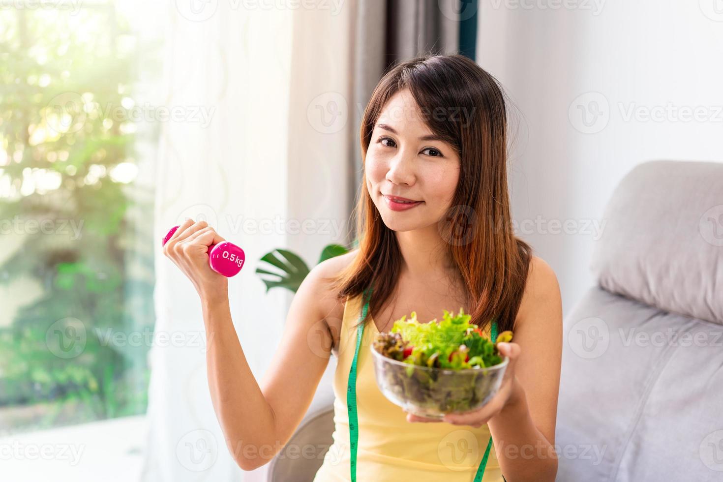 junge frau mit hausgemachtem gesundem salat, der zu hause mit hantel trainiert, gesunder essenslebensstil und diätkonzept foto