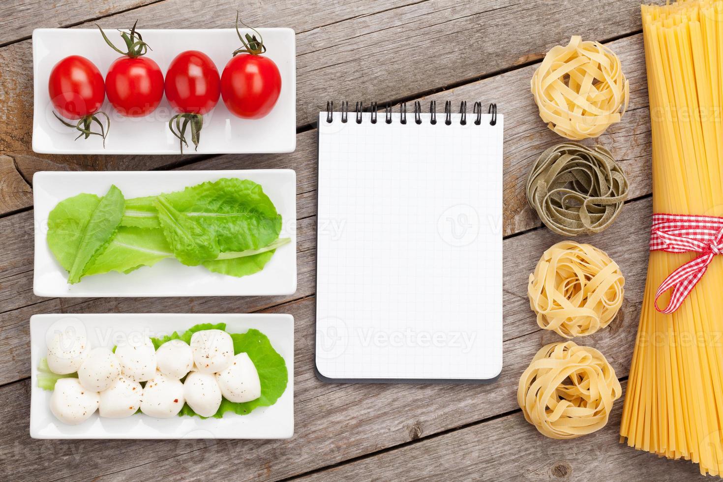 Tomaten, Mozzarella, Nudeln und grüne Salatblätter mit Notizblock foto