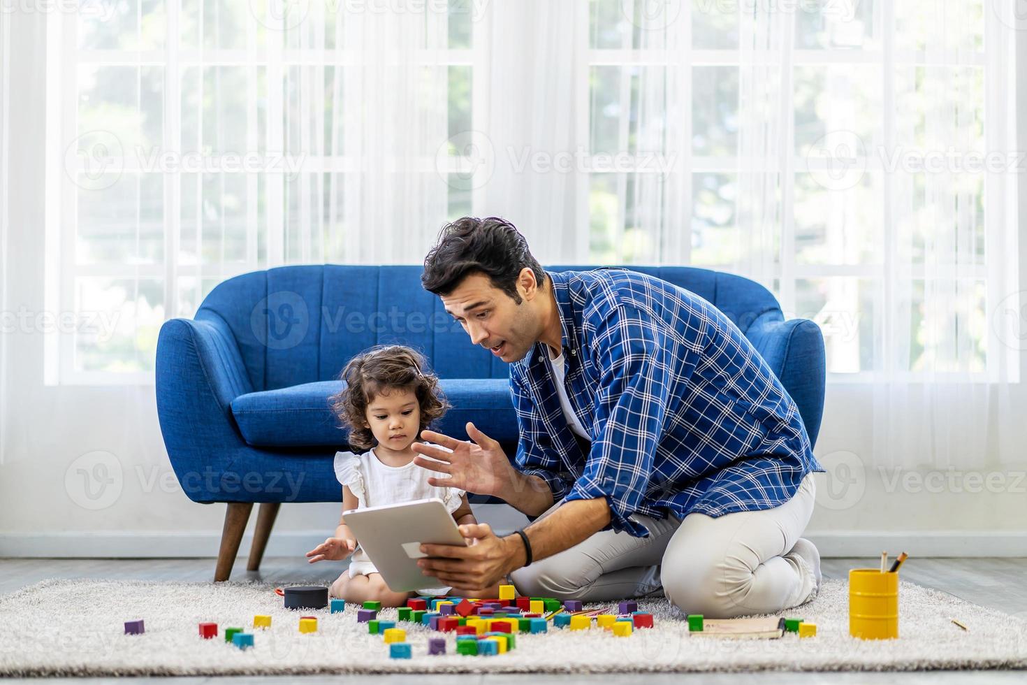 modernes Fernkommunikationskonzept. Porträt eines positiven kaukasischen Vaters, der einen virtuellen Videoanruf mit der Mutter über ein Tablet macht, während die kleine Tochter mit bunten Holzklötzen spielte foto