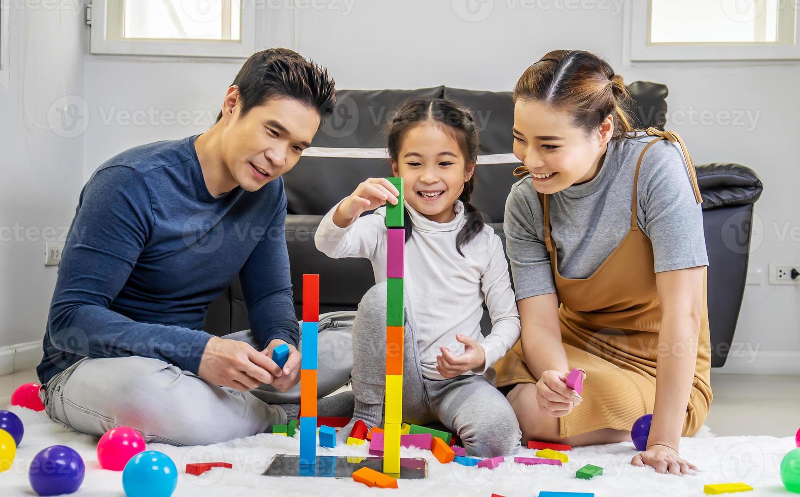 Familien- und Kindheitskonzept. junge familie verbringt zeit im spielzimmer. asiatischer vater, mutter und tochter sitzen auf dem boden und spielen mit bunten blöcken foto